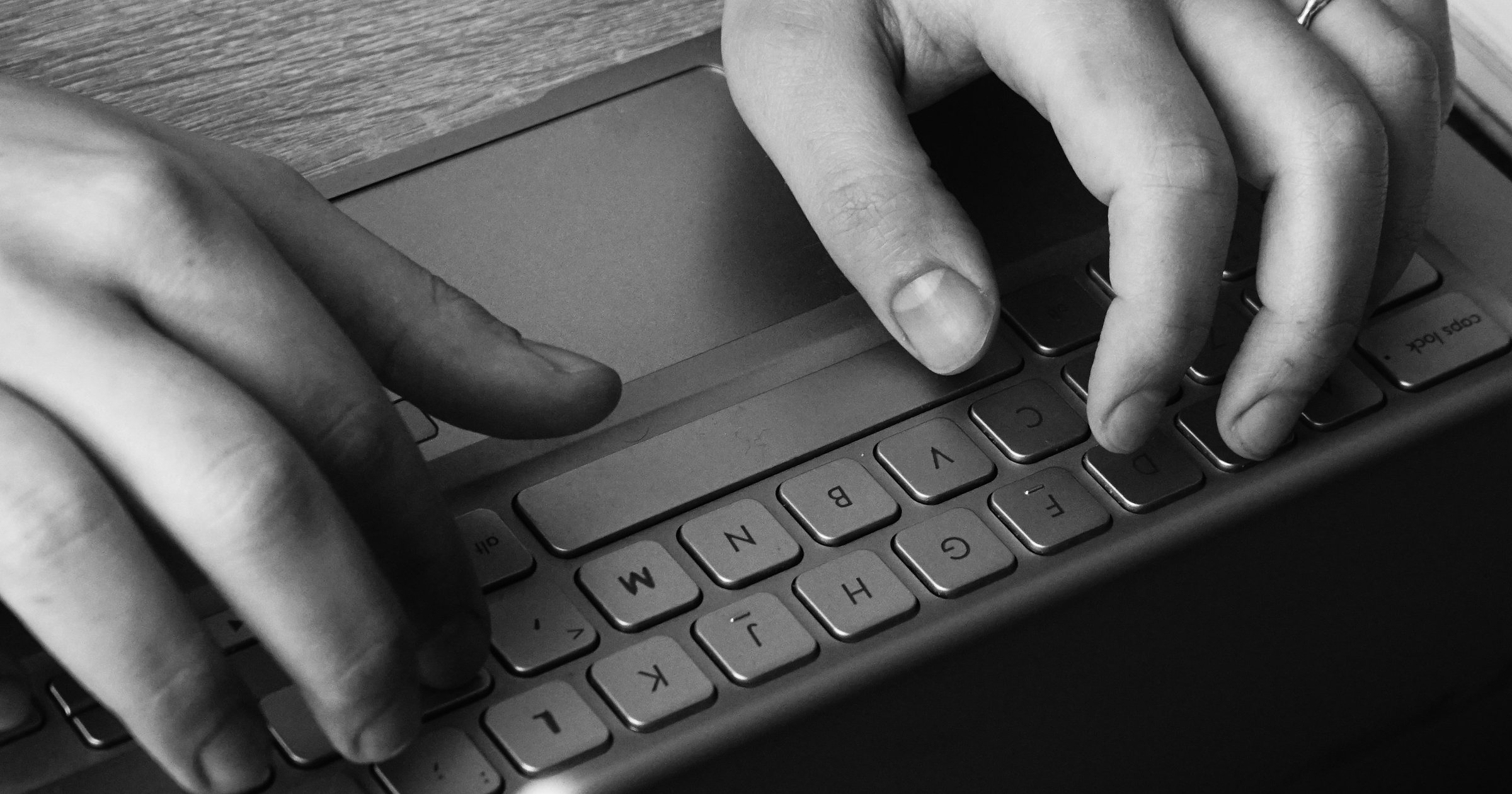 Close-up of hands at a laptop keyboard and trackpad, in black and white